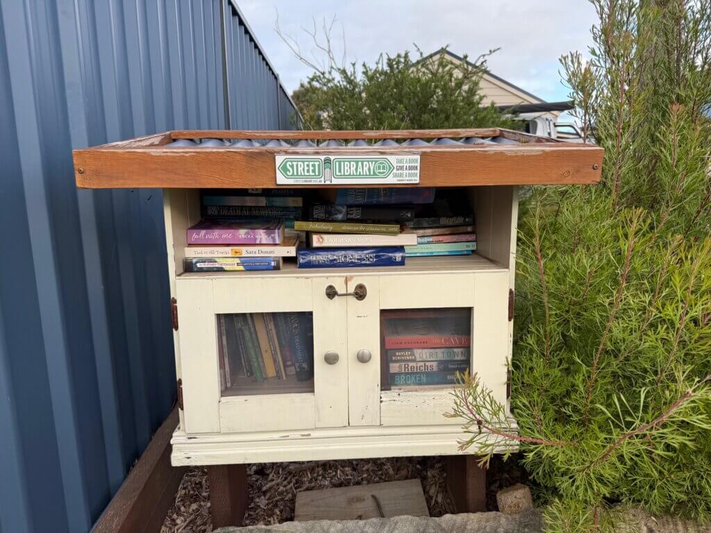 Old wooden cupboard styled as a street library, with door closed.