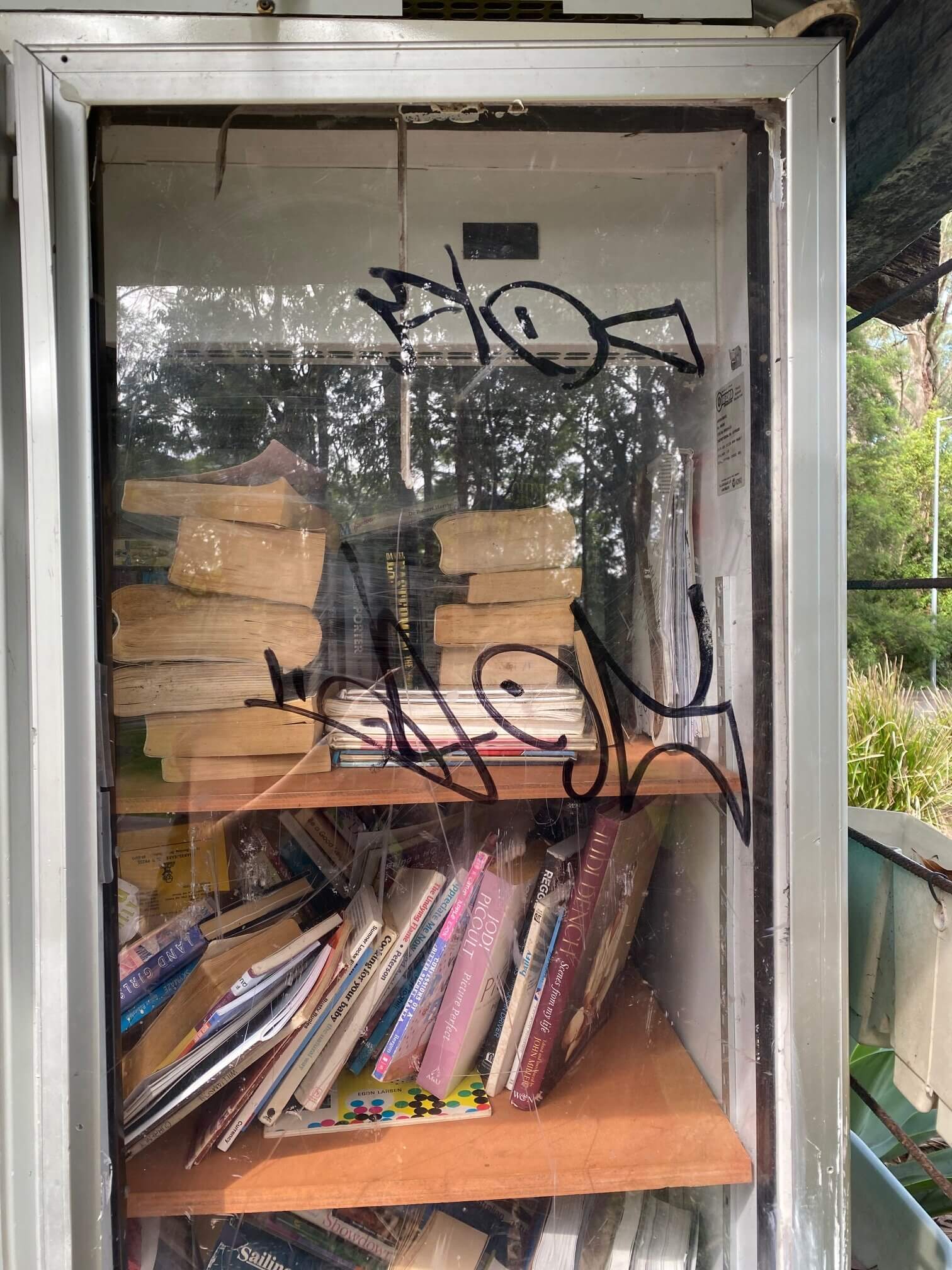 Old fridge styled as a street library with graffiti tags.